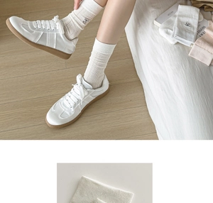 Close-up of white rib-knit calf socks with black bow embroidery and retro GAT sneakers