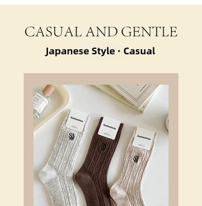 Close-up of cable-knit cotton mid-calf socks with letter embroidery in earth tones
