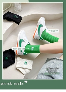 Détail de chaussettes mi-hautes côtelées en vert, noir et blanc avec lettres brodées