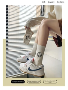 Close-up of white ribbed cotton socks featuring black embroidered smiley faces on high cuffs