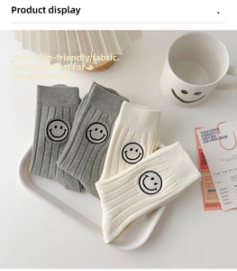Detail of grey and beige ribbed mid-calf socks with smiling face embroidery on white tray
