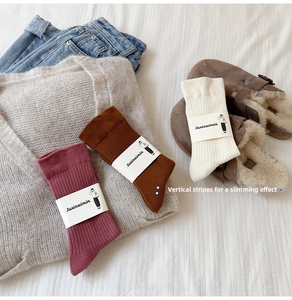 Detail of vertical ribbed cotton socks in burgundy and tan with branded paper packaging
