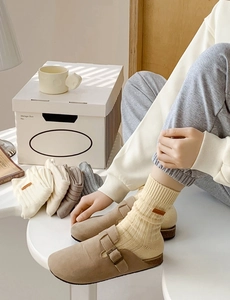 Detail shot of knitted crew socks with leather labels in earth tones on a white box