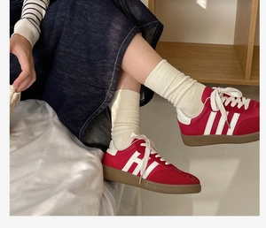 Close-up of red suede retro sneakers with white stripes and gum rubber outsole on feet