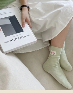 Detail of light green ribbed cotton sock with Hello Nice Day woven label decoration