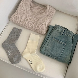 Flat lay of cream cable knit sweater with blue jeans and ribbed crew socks set