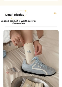 Detail view of cream-colored mid-calf socks with cherry embroidery and ruffled ribbed cuffs