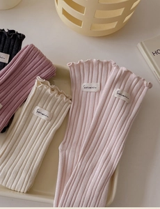 Close-up of pastel knitted socks with ruffle cuffs and woven label on beige tray