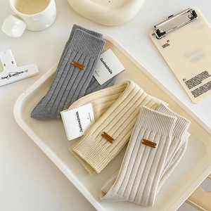 Three pairs of ribbed knit mid-calf socks in grey, beige, and white with leather labels
