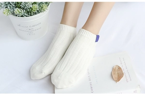 Detail of white rib-knit low-cut cotton socks with a purple decorative fabric label