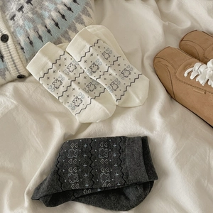 Tre paia di calzini in maglia con motivi di orsi e cuori su sfondo bianco di un letto