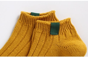 Close-up of ginger yellow ribbed knit cotton ankle socks with green fabric label detail