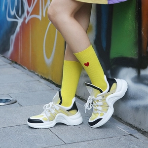 Baskets chunky avec chaussettes jaunes à cœur devant un mur de graffitis