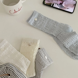 Three pairs of ribbed knit crew socks in blue, white, and beige with button accents