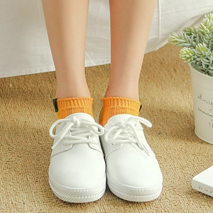 Orange ribbed crew socks with brand label paired with white leather sneakers on a rug