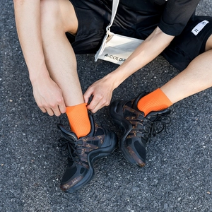 Street style shot of men's bright orange ribbed cotton socks with black monogram sneakers