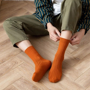 Orange ribbed cotton crew socks for men worn with green pants on wooden floor