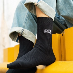 Black cotton crew socks with white embroidered patch on a yellow industrial background