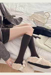 Detail of brown knitted knee-high wool socks with ribbed texture and white plush slippers