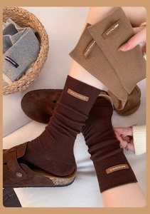 Detail of knit slouch socks featuring lettered leather tags and fine ribbed texture