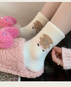 Close-up of pink fluffy slippers and cream socks with cute brown bear patterns