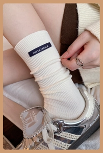 Detail of white ribbed cotton socks featuring a black SUSTAINABLE patch and trendy texture