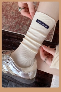 Close-up of cream ribbed cotton socks with navy sustainable label and silver sneakers