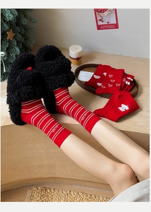 Cozy festive red socks and black plush slippers in a warm Christmas setting