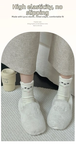 Close-up of white cat-themed fuzzy socks featuring 3D ears and cute facial embroidery