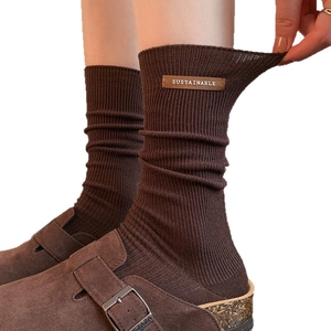 Brown ribbed slouch socks with leather tag paired with suede clogs on white background