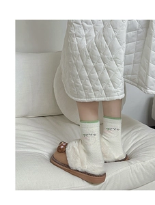 Detail of cozy winter set featuring bear slippers and thick warm white socks on sofa
