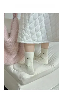 Detail of cream fuzzy socks featuring Happy lettering and cute cartoon face embroidery