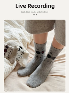 Close-up of gray knit wool socks featuring a black bow pattern and red embroidery detail