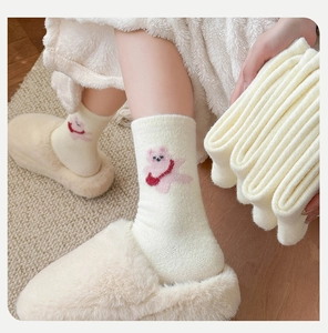Détail de chaussettes pelucheuses blanc cassé avec broderie ours rose et texture douce