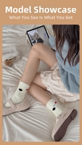 Detail of warm off-white crew socks with cartoon embroidery and plush slippers on a bed