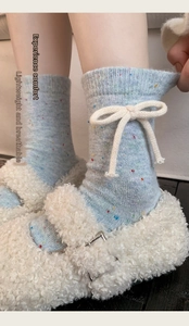 Close-up of light blue wool socks with white bow detail and fuzzy fleece slippers