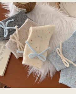 Close-up of thick wool socks with colorful speckled yarn and cute bow ties on soft plush rug