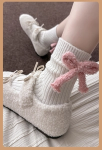 Detail of white wool socks featuring a plush pink bow accent and warm cream home shoes