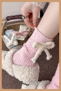 Detail of pink knitted wool socks featuring a fluffy plush bow accent and vertical texture