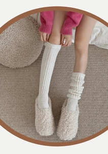 Detail of cream cable-knit wool leg warmers paired with fluffy fleece slippers for home