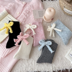Wool blend mid-calf socks with plush bows in five pastel colors on a soft white rug
