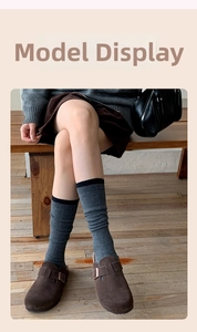 Close-up of grey knit wool socks with black trim styled with brown suede mules