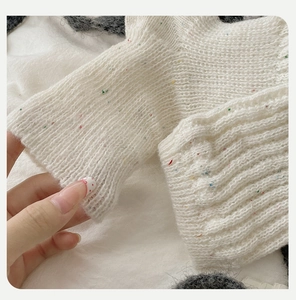 Detailed macro view of cream-colored thick knit wool leg warmers with colorful yarn flecks