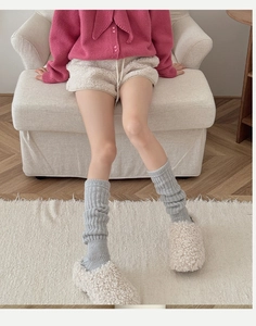 Detail of wool leg warmers in grey vertical knit paired with fluffy slippers