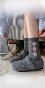Détail de chaussettes en laine à losanges gris avec chaussures Mary Jane sur tapis blanc