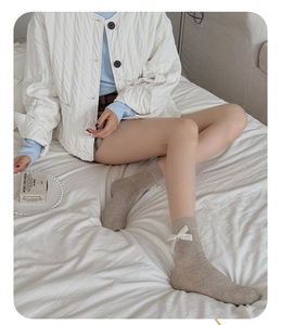 Détail de chaussettes en coton côtelé beige avec un élégant nœud en dentelle blanche