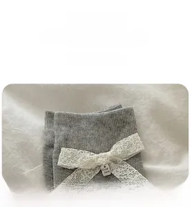 Détail de chaussettes en coton gris avec nœud en dentelle blanche et pendentif Good Luck