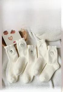 Close-up of five pairs of white plush thermal socks with colorful bow embroidery details