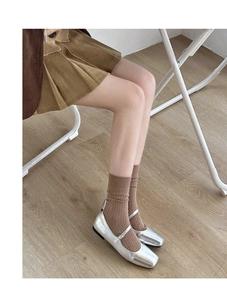 Detail of silver metallic Mary Jane flats with brown ribbed socks on wooden floor