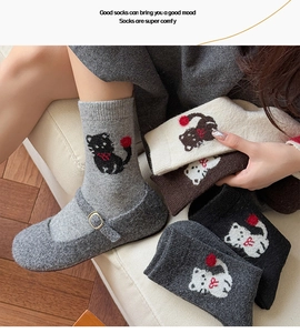 Nahaufnahme der Wintersocken mit Katzen-Jacquardmuster und roten 3D-Pompons aus Strick